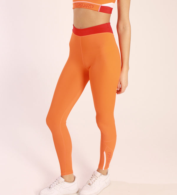 Eine Frau trägt eine orange Sportleggings mit einem roten Bund und einem  Bodyguard-Logo am Bein unten