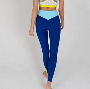 Eine Frau trägt eine dunkelblaue Sportleggings mit einem hellblauen Bund und einem gelben Akzentstreifen mit Bodyguard-Logoam Bein unten