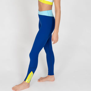 Eine Frau trägt eine dunkelblaue Sportleggings mit einem hellblauen Bund und einem gelben Akzentstreifen mit Bodyguard-Logoam Bein unten